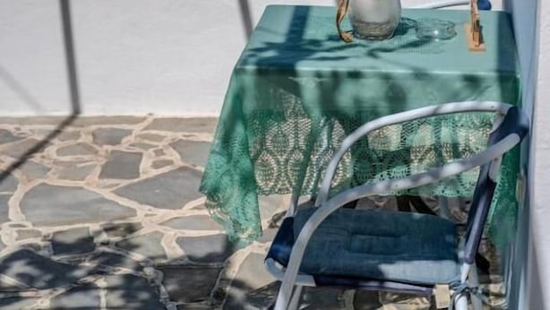 A table with a green tablecloth and a pitcher on it, set on a stone floor with a view of the sea. - Irene's Cottage Myrtonas (Karpathos)