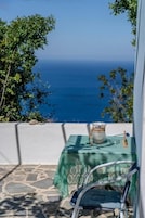 Una mesa con mantel verde y una jarrón, sobre un suelo de piedra con vista al mar.