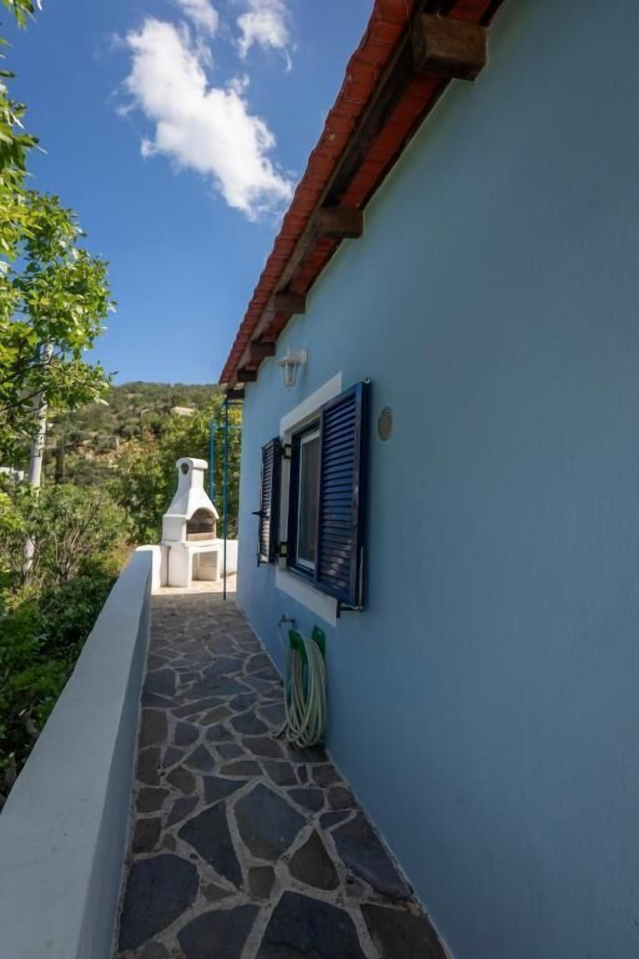 Un étroit sentier pavé de pierres mène à un bâtiment dont le mur est bleu et le toit rouge.