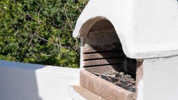 Un horno de piedra blanco con base de ladrillo, frente a un fondo de vegetación y el mar.