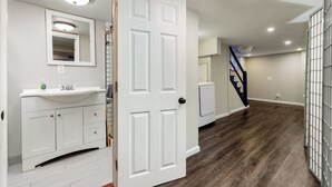 A hallway with a white door, a white vanity with a mirror, and a staircase in the background. - Beautiful 3 Story Home in Best Tower Grove Location (St. Louis)