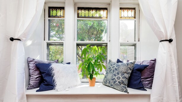 A window seat with a potted plant, patterned pillows, and a white curtain. - Beautiful 3 Story Home in Best Tower Grove Location (St. Louis)