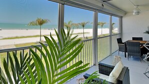 Een balkon met uitzicht op het strand, rieten meubilair en een plafondventilator.