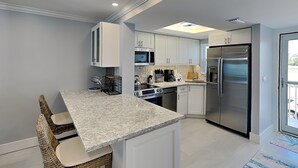 Een moderne keuken met witte kastjes, een granieten aanrechtblad, roestvrijstalen apparatuur en een eethoek met rieten stoelen.