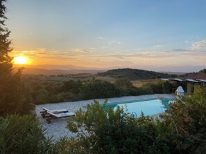 Une piscine entourée de chaises longues, de verdure et offrant une vue sur des collines lointaines.