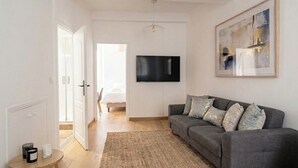 Ett modernt vardagsrum med en grå soffa, en väggmonterad TV, en inramad abstrakt målning och ett trägolv.