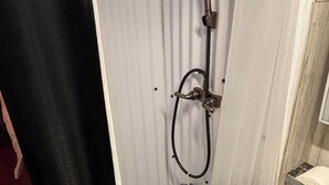 Een kleine, afgesloten douchecel met douchekop en een handdouche, en een toilet.