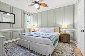 Ein Schlafzimmer mit Bett, Nachttisch, Lampe, Deckenventilator und Fenster.