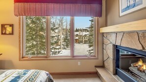 Ein Zimmer mit großem Fenster, Kamin und einem Bett mit gemustertem Überwurf.