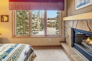 A room with a large window, a fireplace, and a bed with a patterned bedspread. - Ski-in/out|Free Shuttle|Private Hot Tub|Garage (Breckenridge)
