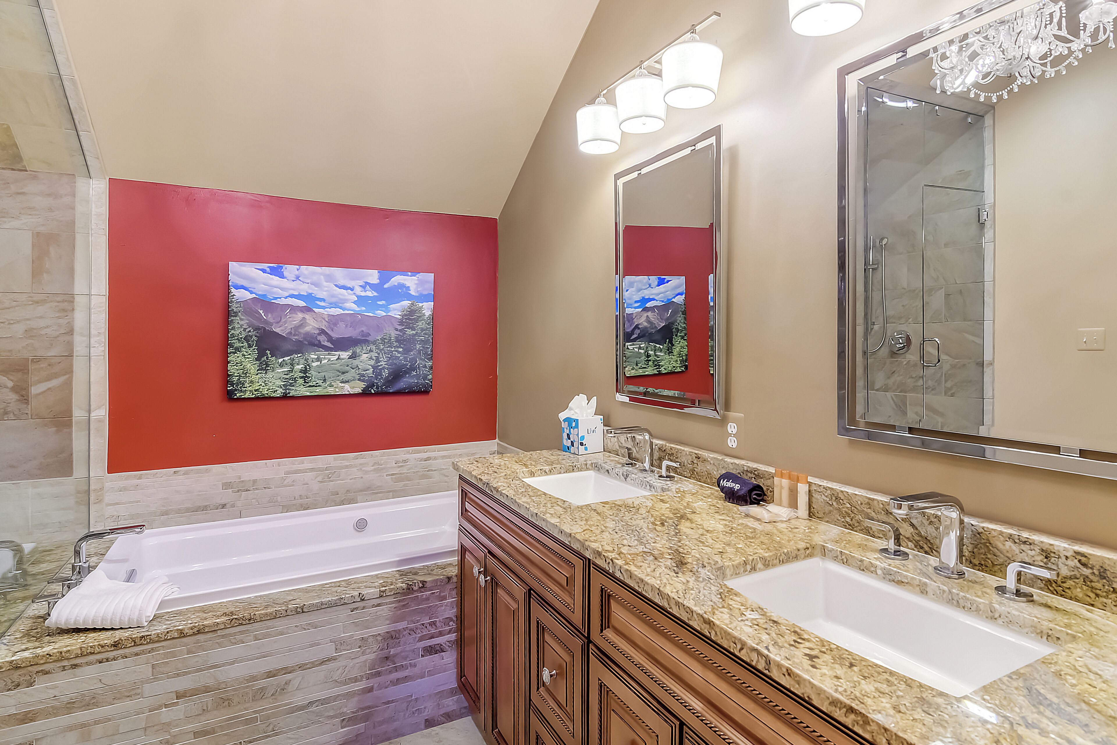 A bathroom with a large tub, two sinks, a shower, a red accent wall, and a large mirror.