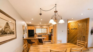 Un comedor con una mesa y sillas de madera, una cocina al fondo y una puerta de madera con un diseño diagonal.