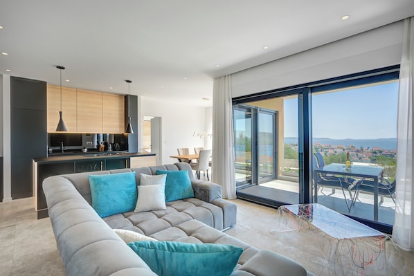 A modern living room with a sofa, a dining table, and a kitchen area. - Luxury apartment with stunning views and pool (Seget Vranjica)