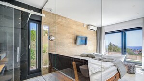 A modern bedroom with a large bed, a TV, and a view of the outdoors. - Luxury apartment with stunning views and pool (Seget Vranjica)