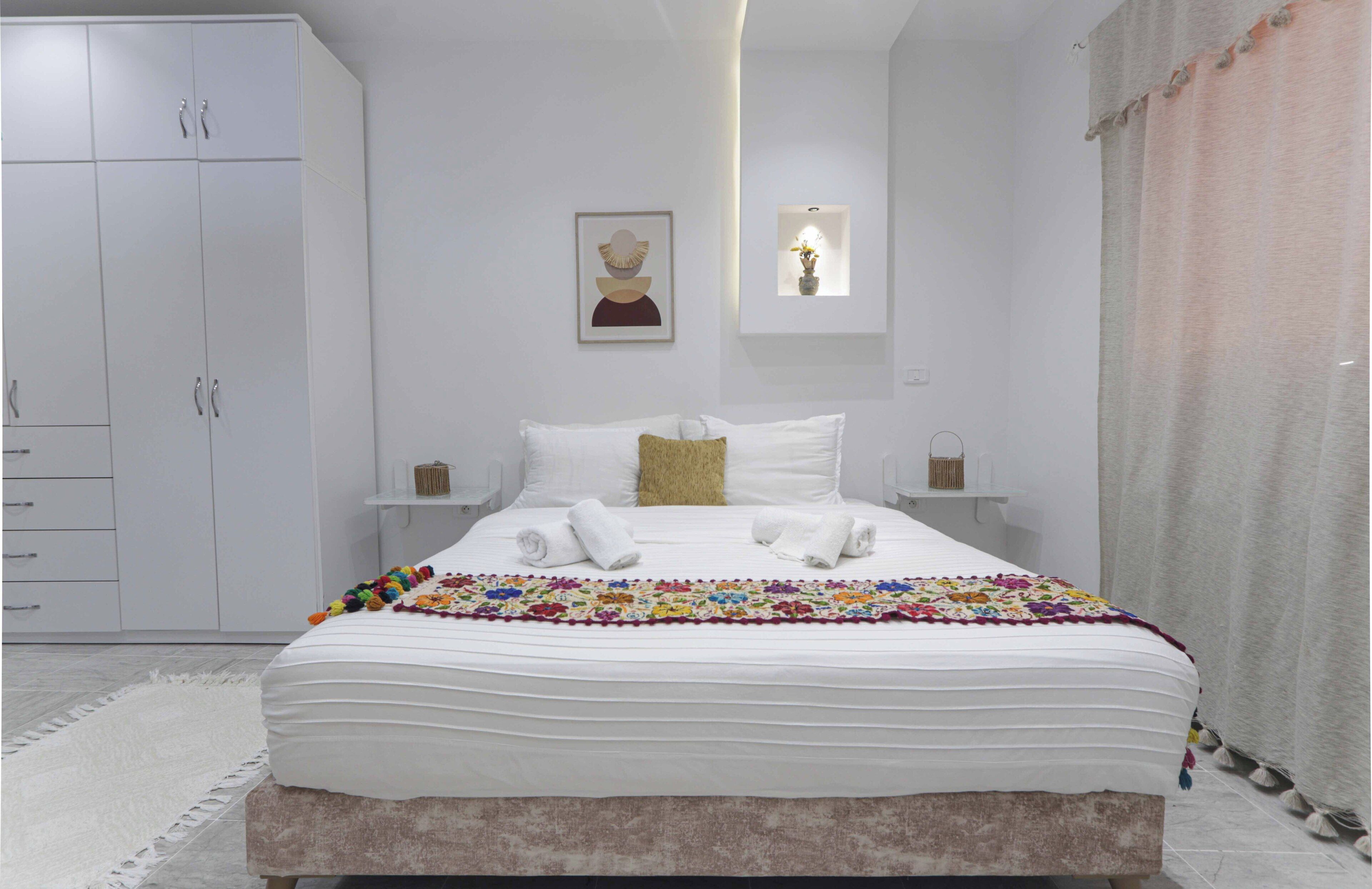 Une chambre bien rangée, avec un grand lit, une armoire et une table de chevet sur laquelle se trouve une lampe.