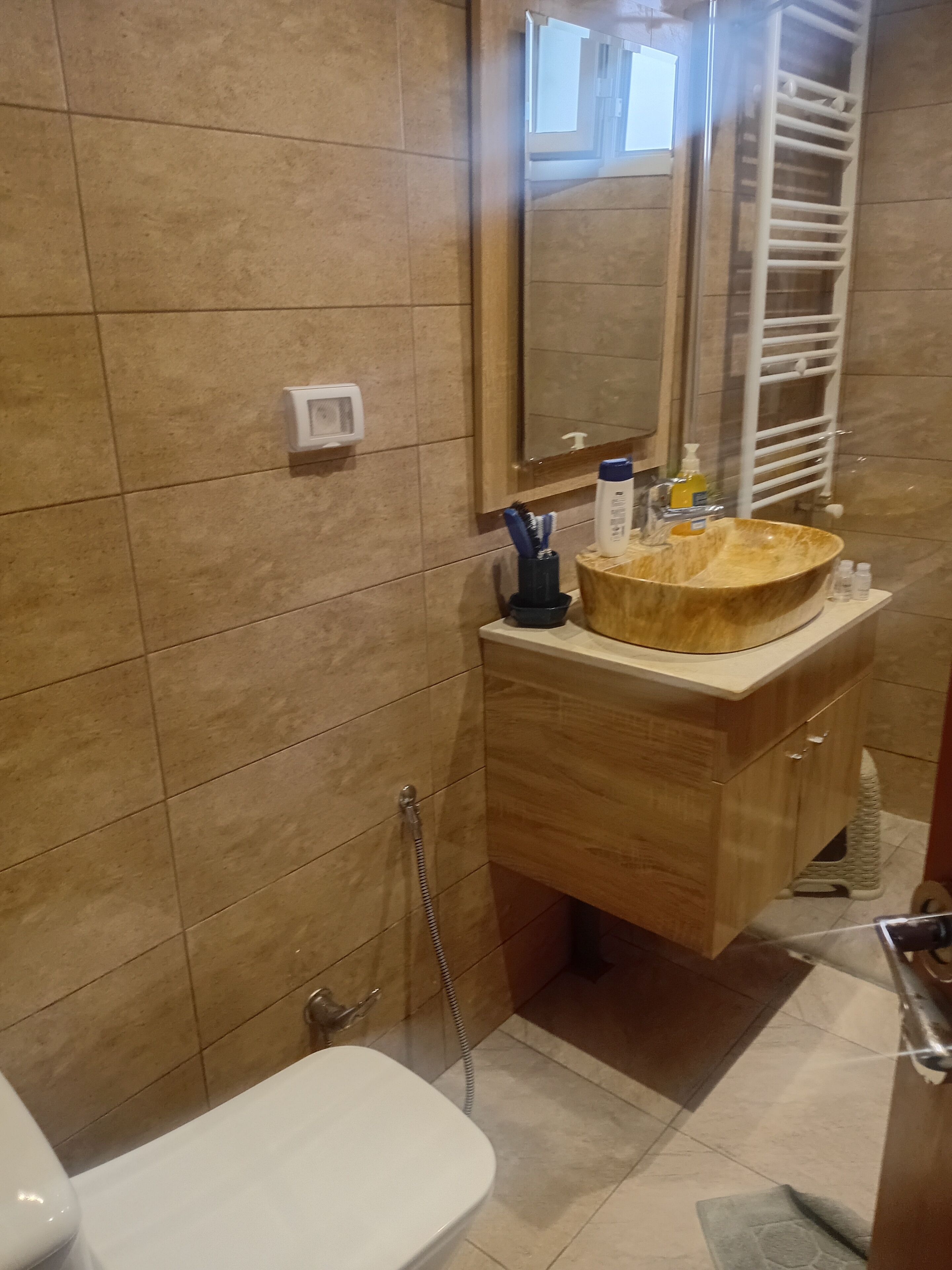 A bathroom with a wooden vanity, a large mirror, a white sink, and a shower area.