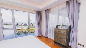 A bedroom with a large bed, a dresser, and a view of a body of water and buildings. - ANGSANALUXUREAPR (Thalang)