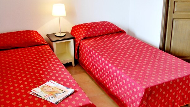 A room with two single beds, a nightstand with a lamp, and a magazine on the floor. - Cosy Village Studio Retreat in Barjac (Barjac)