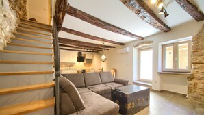 Una sala de estar moderna con sofá, una escalera de madera, una zona de cocina y una pared de piedra.
