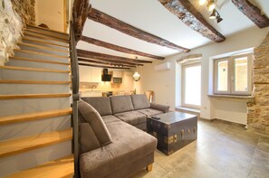 A modern living room with a sofa, a wooden staircase, a kitchen area, and a stone wall. - Vacation home Domagoj with Jacuzzi (Vrbnik)