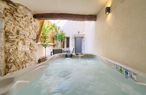 A hot tub in a narrow space with stone walls, a wooden beam ceiling, and a door in the background. - Vacation home Domagoj with Jacuzzi (Vrbnik)