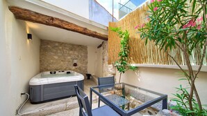 Un jacuzzi, una mesa de vidrio con sillas y una celosía de bambú en un espacio exterior con paredes de piedra.