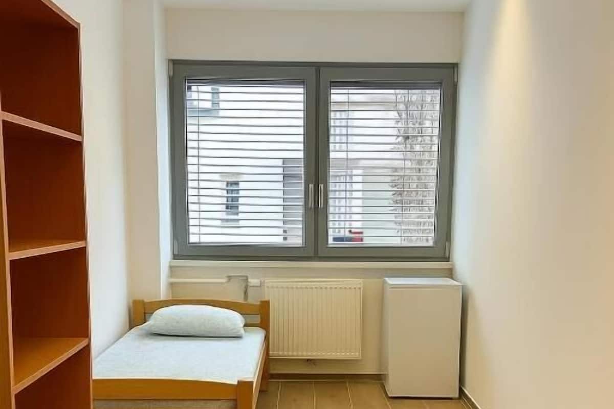 A bedroom with a bed, a radiator, a window with blinds, and a wooden wardrobe.