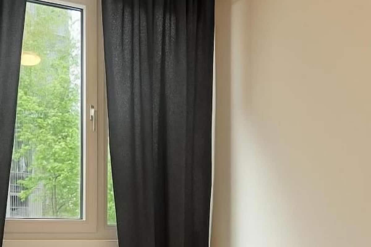 A single bed with a patterned bedspread, a window with curtains, and a radiator.