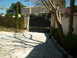 A gated entrance with a stone wall, a paved driveway, and a tree with flowers. - Ground floor apartment facing the swimming pool, private property and parking on enclosed grounds (Salon-de-Provence)