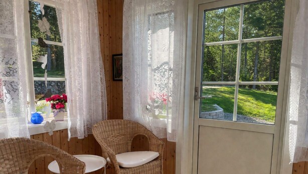 A room with wicker chairs, a window with lace curtains, and a view of a green landscape. - 4 Person Holiday Home in Uddevalla (Uddevalla)