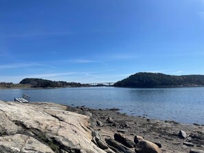 A rocky shoreline with a bridge in the distance, a clear sky, and a forested island. - 4 Person Holiday Home in Uddevalla (Uddevalla)