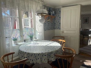 Ein Essbereich mit einem runden Tisch, Stühlen, einem Fenster mit Spitzgittervorhängen und einer Wand mit Muster.