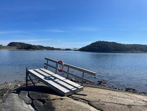 A wooden dock with a lifebuoy, a clear blue sky, calm water, and a forested hill in the background. - 4 Person Holiday Home in Uddevalla (Uddevalla)