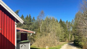 A red building with a small attached structure, a gravel path, and a forested area. - 4 Person Holiday Home in Uddevalla (Uddevalla)