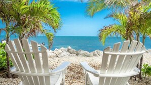 Two white Adirondack chairs facing a beach with a clear blue sky and palm trees. - Open Ocean, Sunrise and Moonrise. Tropical fish and Seabirds at your fingertips! (Duck Key)