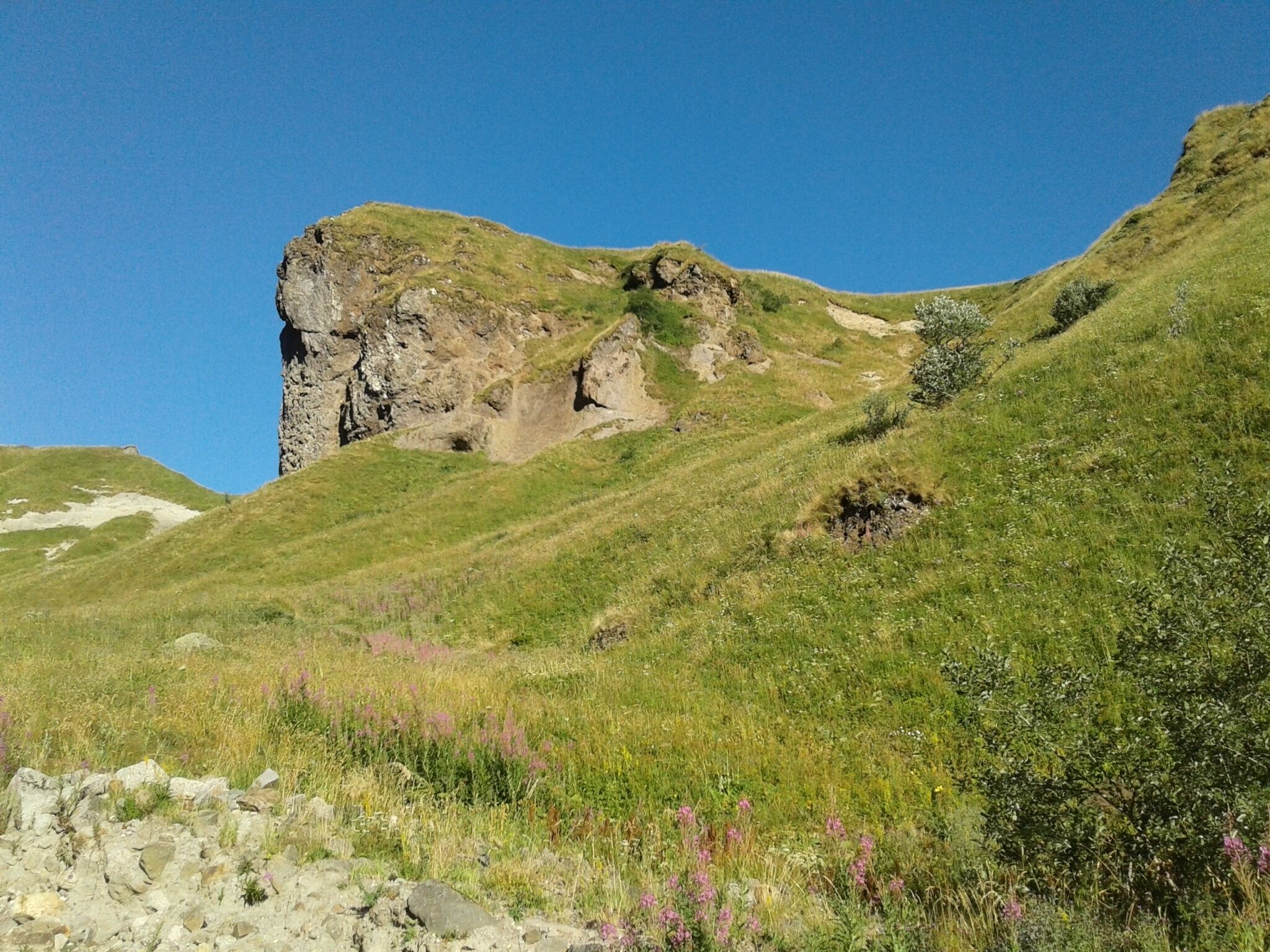 A rocky hill with a grassy slope and a clear blue sky.