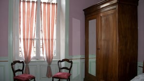 A room with two wooden chairs, a wooden wardrobe, and a window with curtains. - Character apartment (Mont-Dore)
