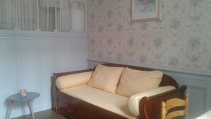 A room with a wooden sofa, a small round table, and a floral wallpaper. - Character apartment (Mont-Dore)