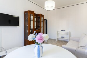 Ein modernes Wohnzimmer mit Flachbildfernseher, einem Holzschrank, einem weißen runden Tisch mit Blumen und einem weißen Sofa.