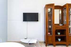 Ein Zimmer mit Flachbildfernseher an der Wand, einem weißen Tisch mit Stuhl und einer Holzvitrine.