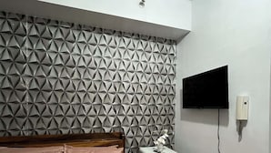 Ein Schlafzimmer mit einem Bett, einem kleinen, weißen Kühlschrank, einem an der Wand montierten Fernseher und einer Wand mit einem geometrischen Muster.