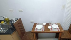 Ein kleiner Essbereich mit einem Holztisch, gedeckt für zwei Personen, eine Küche mit Spüle und Kochutensilien sowie ein Heizkörper an der Wand.
