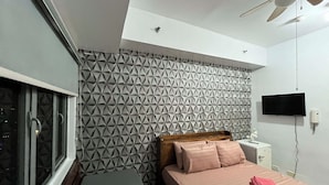 Ein Schlafzimmer mit Bett, Fenster, Deckenventilator, Fernseher und einem kleinen weißen Gerät.