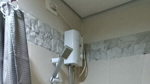 Eine Dusche mit Handbrause, Bedienfeld an der Wand und Duschvorhang.