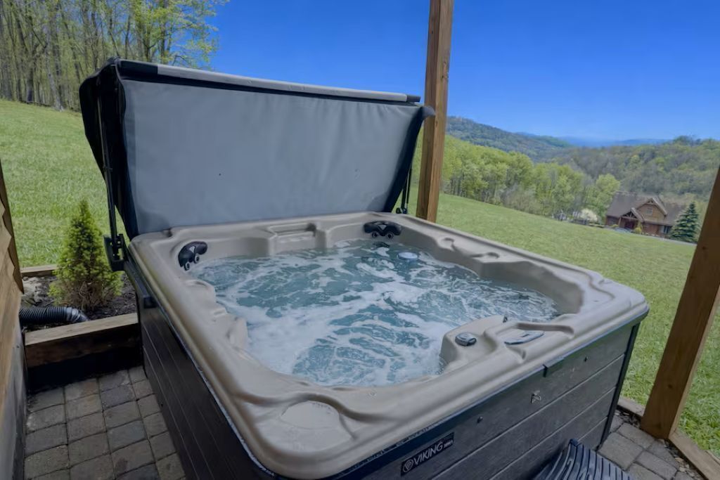 A hot tub with a wooden deck and a scenic view of a house and mountains.
