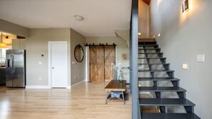 Et moderne køkken med et rustfrit stål køleskab, et træspisebord med en vase, og en trappe med et unikt design.