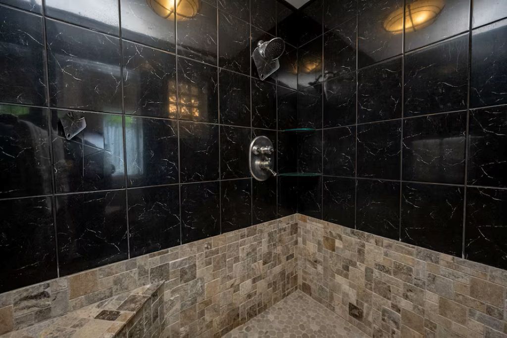 A bathroom with black marble tiles, a shower, and a tiled floor.