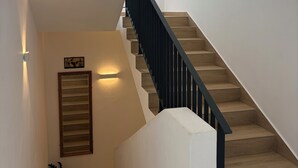 A modern staircase with wooden steps and a black railing, leading to a landing with a light fixture and a framed picture. - J'Vais Residence Flic en Flac (Flic en Flac)