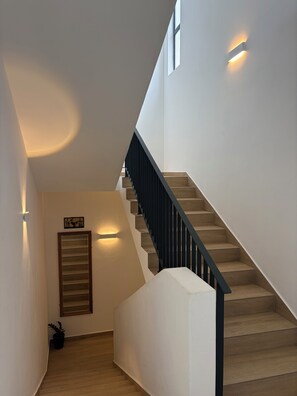 Una escalera moderna con escalones de madera y barandilla negra, que conduce a una plataforma con una lámpara y un cuadro enmarcado.