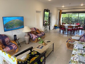 A living room with a television, sofa, chairs, a table, and a dining area with chairs and a table. - J'Vais Residence Flic en Flac (Flic en Flac)